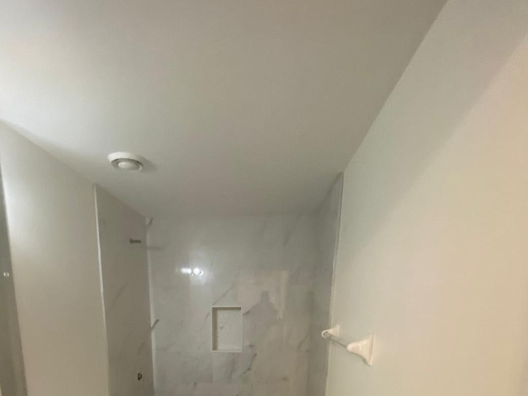 White painted walls and ceiling around a marble-look tiled tub alcove in a basement bathroom