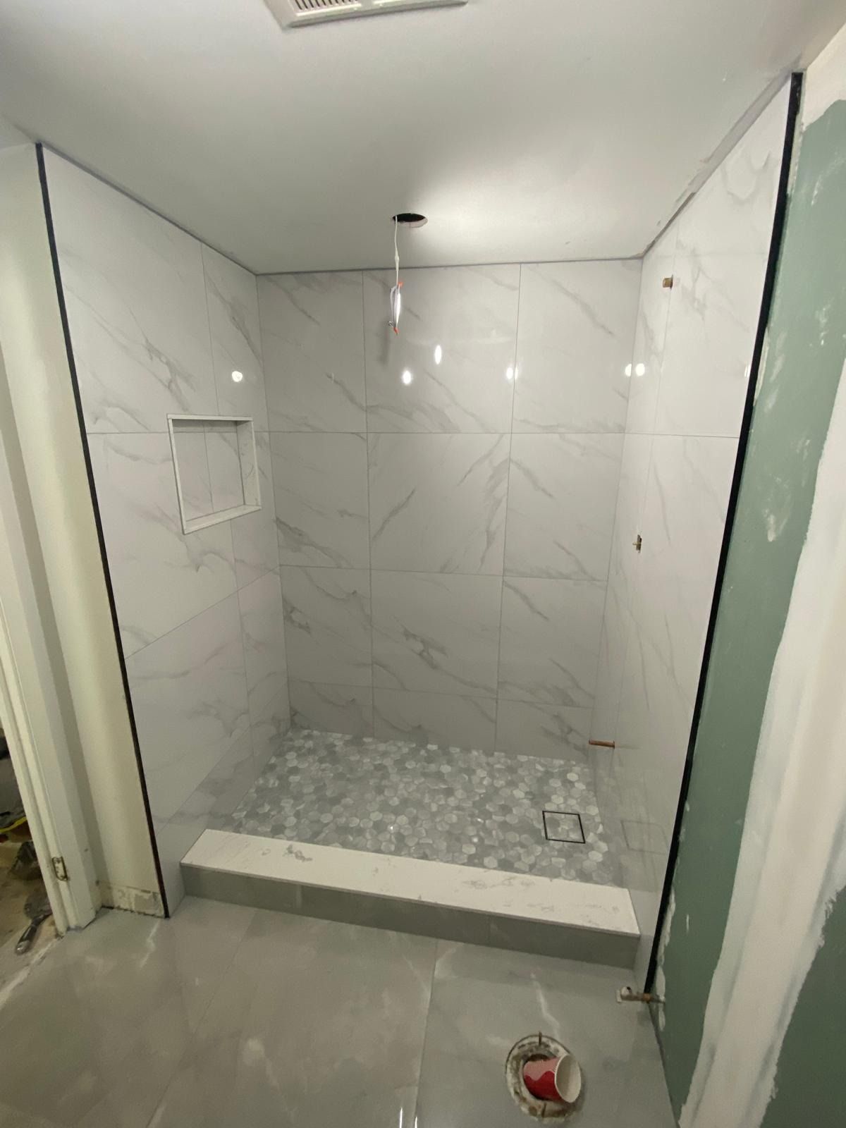 Curbed shower with marble-look wall tile, a grey hex mosaic floor and a niche